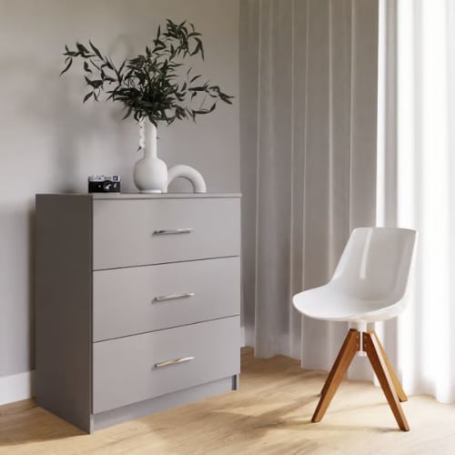 Gray chest of drawers with silver handles, styled with a white vase, greenery, and a camera, next to a white chair