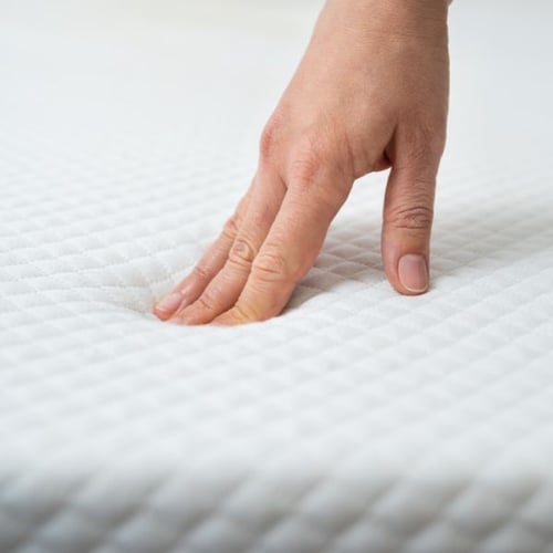 Hand pressing into soft, supportive mattress surface
