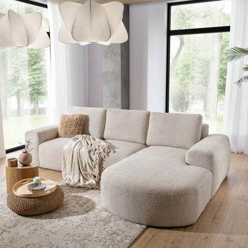 Nowoczesna beżowa narożna sofa z zaokrąglonym szezlongiem w stylu boucle w jasnym salonie z dużymi oknami – best corner sofa do przytulnego wnętrza.