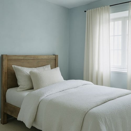Light blue-toned bedroom featuring a wood-frame bed with white bedding and curtains